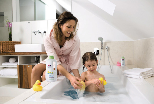 Child in bathtub playing with duck, mother in bathrobe on edge of tub